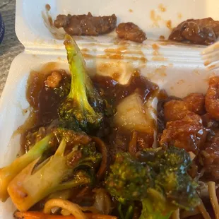 a close up of a take out container with noodles, broccoli and meat