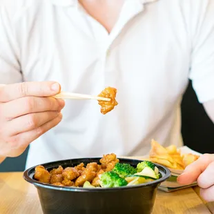a man holding chopsticks over a bowl of food