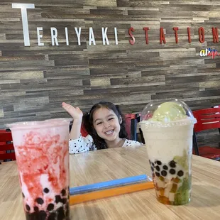 a little girl sitting at a table with two drinks