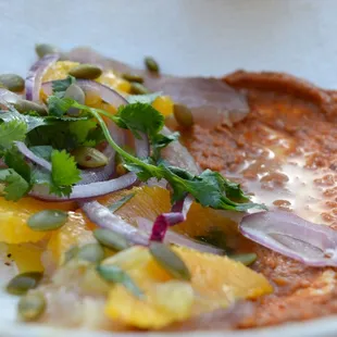 a bowl of food with oranges, onions, and capers