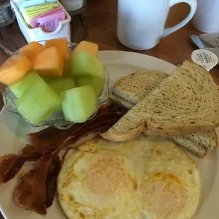 Classic breakfast over medium eggs, bacon, fruit, rye toast.