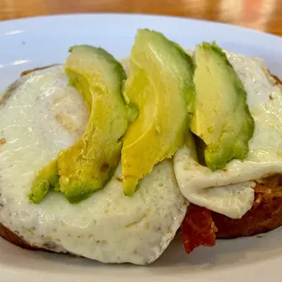 Open faced breakfast sandwich. There's bacon &amp; cheddar below the fried eggs and avocado.