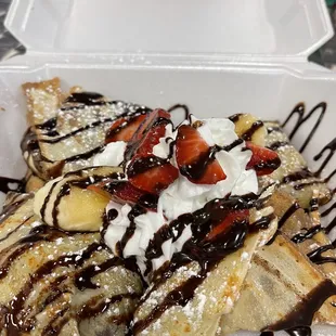 a plate of crepes with whipped cream, strawberries, and chocolate sauce