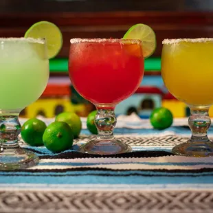 three margaritas on a table with limes