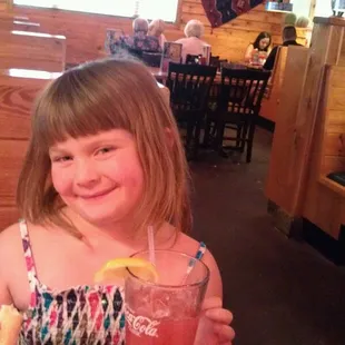 a little girl sitting at a table with a drink