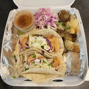 two tacos and potatoes in a styrofoam container