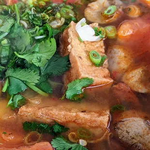 Very close up of Tom yum soup with tofu, with fresh herbs on top. Yum indeed!