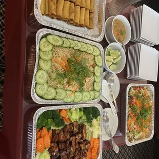 A tray of eggs rolls, pineapple fried rice, chicken teriyaki and drunken noodles.