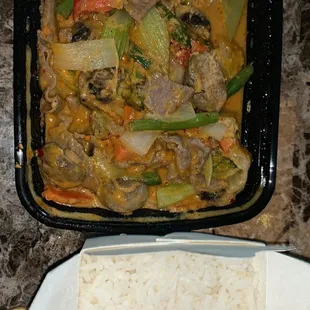a plate of rice and a container of meat and vegetables