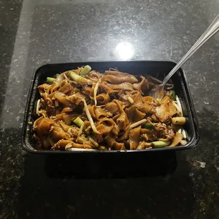 a black container with noodles and meat