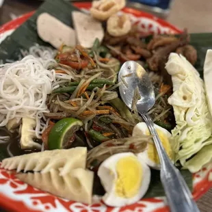 Tum Thard Lao Style papaya salad with boiled egg, moo your, vermicelli noodles, pork rinds, bamboo, and extra crispy chicken pieces.