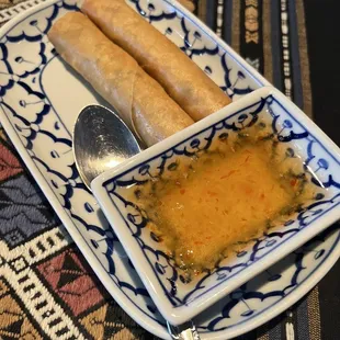a bowl of dipping sauce and two spring rolls
