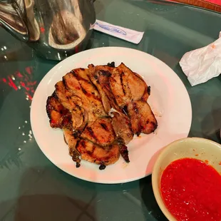 a plate of grilled chicken and a bowl of sauce
