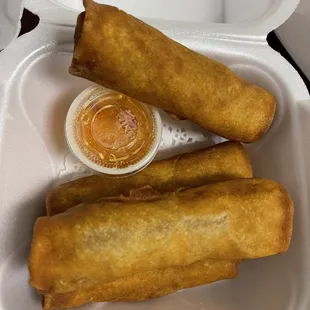 three fried spring rolls in a styrofoam container