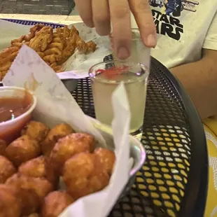 A man grabbing for his yellow shot with waffle fries and sweet potato tots on table