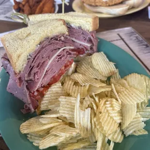 Corn beef, pastrami, and Swiss cheese on a Texas toast, with a side of potato chips