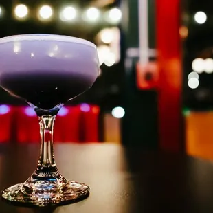 a purple cocktail in a coupe glass