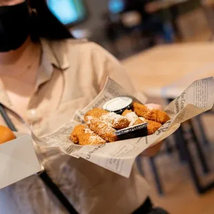 a woman wearing a face mask and holding a tray of donuts