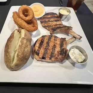 Grilled pork chops with baked potato and onion rings.