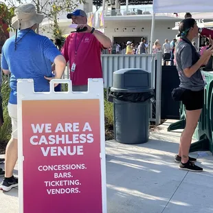 people standing around a sign that says we are a cashless venue