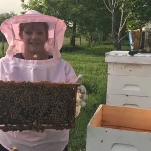 a woman in a bee suit holding a beehive