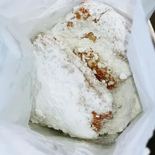 Beignets loaded with powdered sugar in a bag for you to shake.