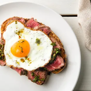 Our Chimmy Steak Toast is topped with a 6oz filet, sunny side up egg, Chimichurri sauce, and your choice of a side.