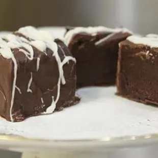 Our Signature Fudge Cakes, a blend of dark chocolate fudge and dark chocolate cake covered in dark chocolate and a white chocolate drizzle.