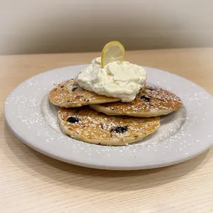 a plate of pancakes with whipped cream and a lemon slice