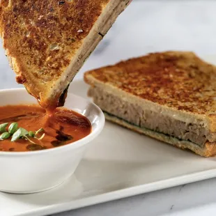 a grilled cheese sandwich being dipped with tomato soup