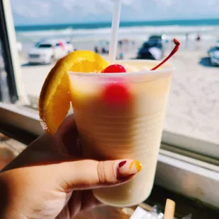 a hand holding a drink with a straw and a slice of orange
