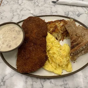 Chicken fried "ribeye" steak with gravy on the side. Sides are scrambled eggs, hash browns, and wheat toast.