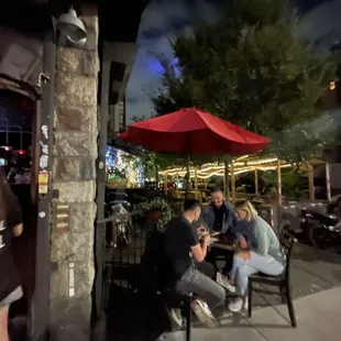 a group of people sitting at a table under a red umbrella