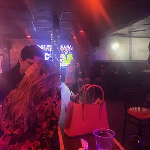 A skinny long bar (no drinks) between the bar (with bartenders) and stage. View of 4 tv&apos;s playing sports.