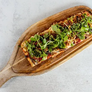 Indulge with our Flatbread with creamy goat cheese, garlic, oak-fired oyster mushrooms, sausage, dried tomato, pistachio, and fresh greens.