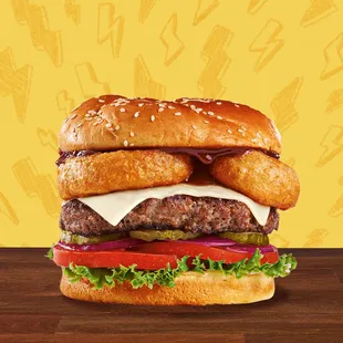 a hamburger with cheese, lettuce, tomato, and onion rings