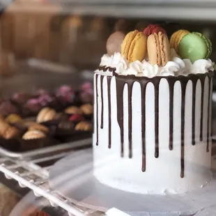 a white cake with chocolate drips and macarons