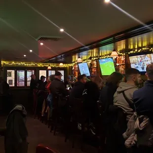 a group of people sitting at a bar watching televisions
