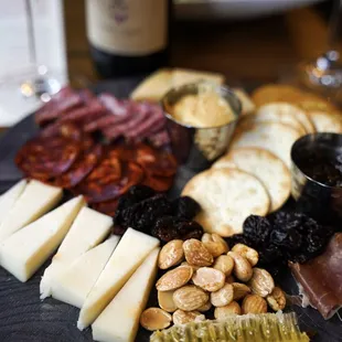 a platter of cheese, crackers, nuts, and wine