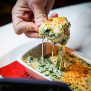 a person dipping a piece of cheese over a casserole dish