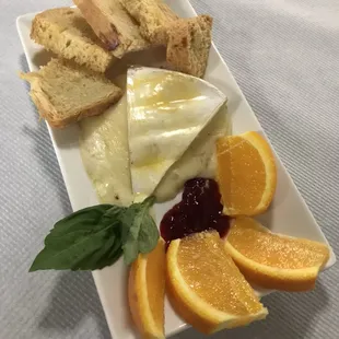 Baked Brie served with raspberry preserves, orange slices, and toasted crustinis