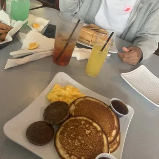 a woman sitting at a table with a plate of pancakes and eggs
