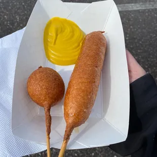 a person holding a basket of corndogs and mustard