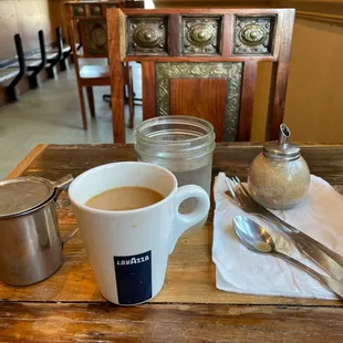 a table with a cup of coffee, spoons, and utensils