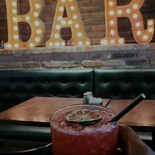 a person holding a drink in front of a bar sign