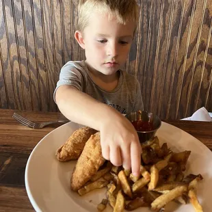 a young boy reaching for a plate of french fries