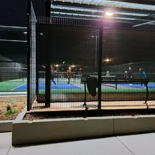 Spectator seating area with bench and paddle rack at each end of 3 courts