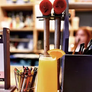 a glass of orange juice and crayons