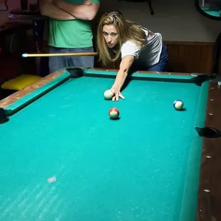 Two patrons playing a game of pool and unwinding from their respective work days. After all, a game of pool is a Universal language