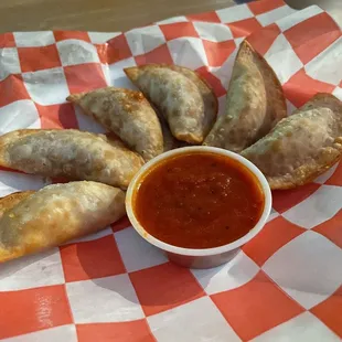 a plate of empanadas and a bowl of sauce